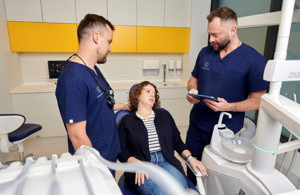 Lekarze dentyści tłumaczący pacjentce co wybrać: implant czy most
