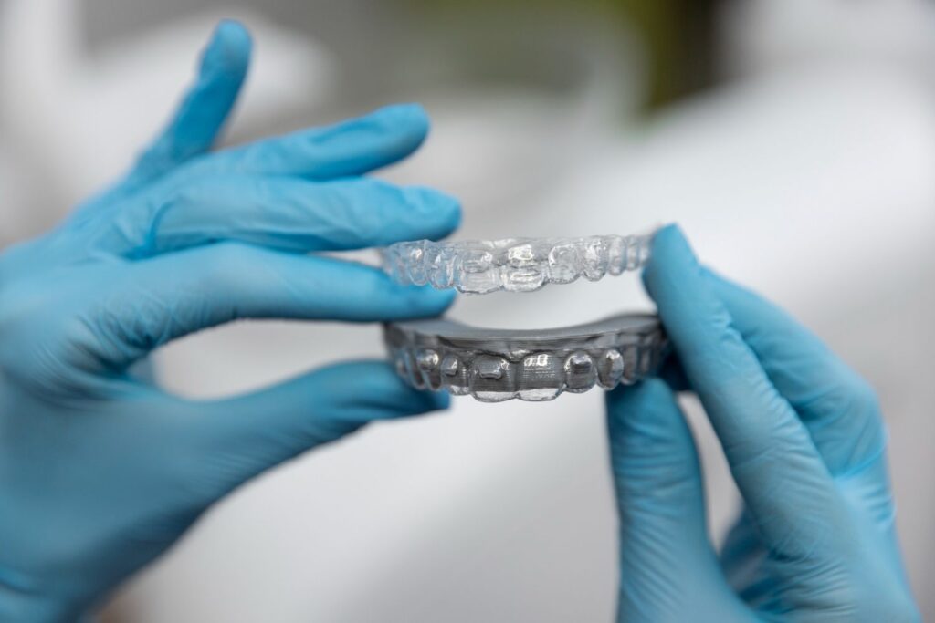 Dłonie w rękawiczkach trzymające przezroczysty aparat na zęby invisalign