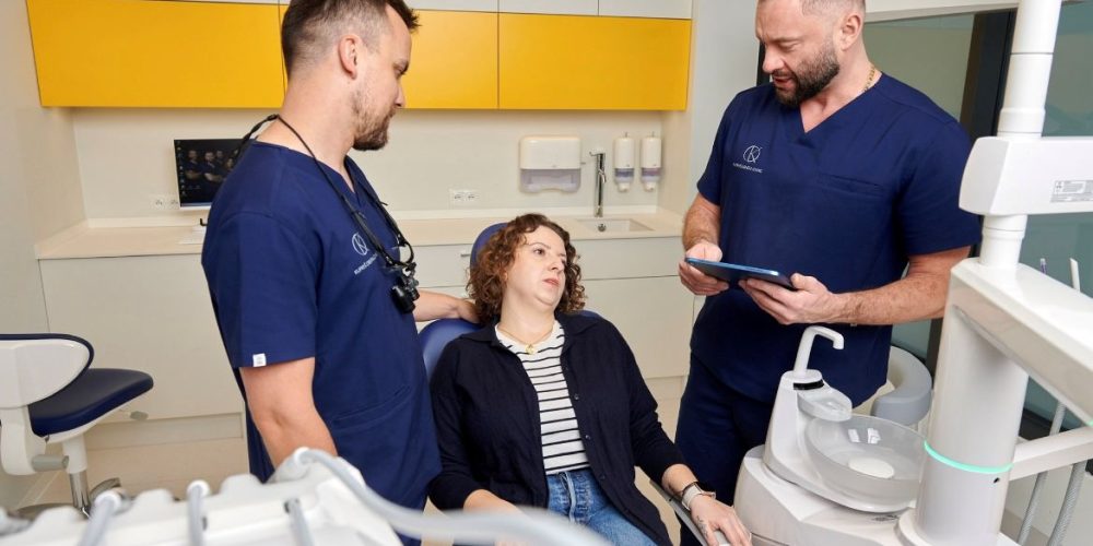 Lekarze dentyści tłumaczący pacjentce co wybrać: implant czy most