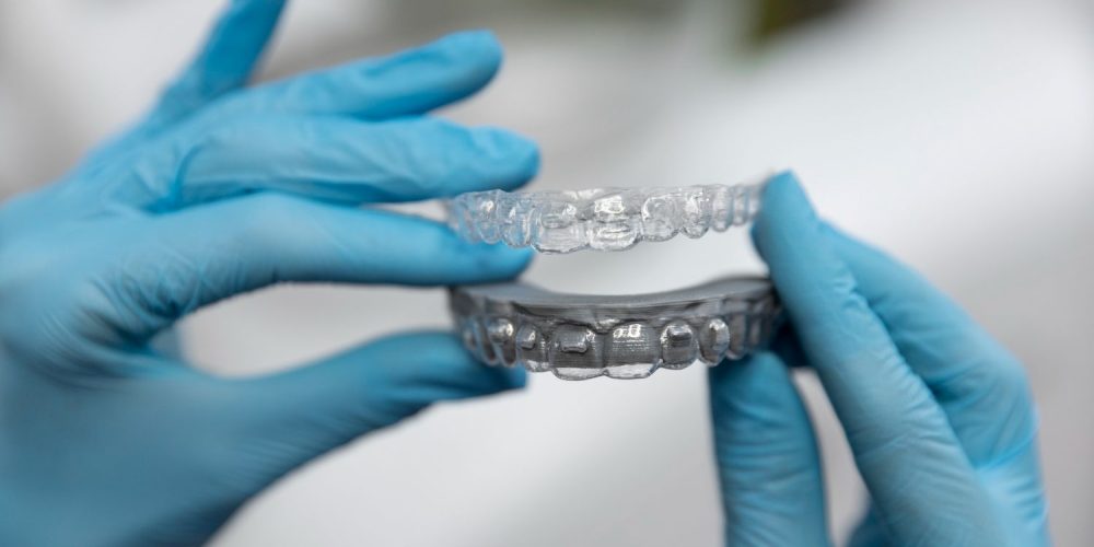 Dłonie w rękawiczkach trzymające przezroczysty aparat na zęby invisalign
